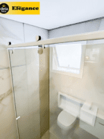 Box Elegance de vidro temperado incolor com estrutura metálica e roldanas aparentes na cor branco, sendo 1 folha fixa e 1 porta de correr.