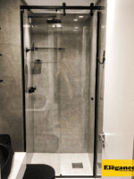 Box Elegance de vidro temperado incolor com estrutura metálica e roldanas aparentes na cor preta, sendo 1 folha fixa e 1 porta de correr.